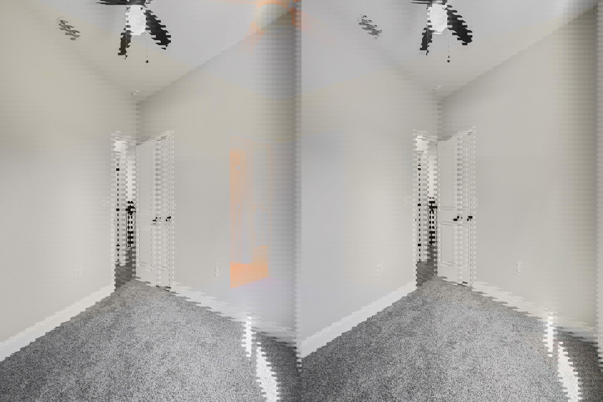 Carpeted room with white paneled door featuring black hardware, ceiling fan with light fixture, and ceiling vent