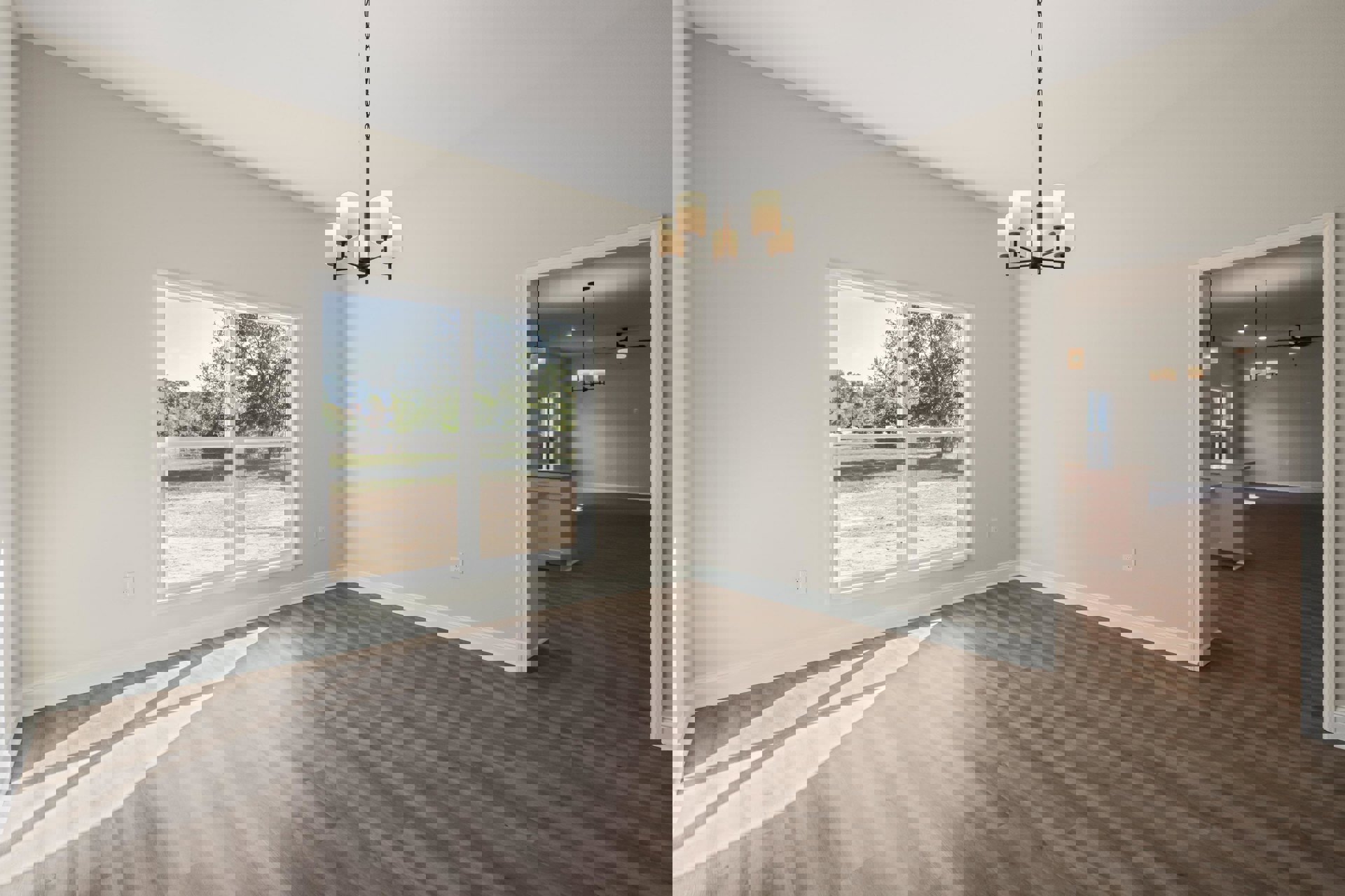 Living room with wide plank wood flooring, white plaster walls, large window overlooking a field and trees, and a modern chandelier with white shades.