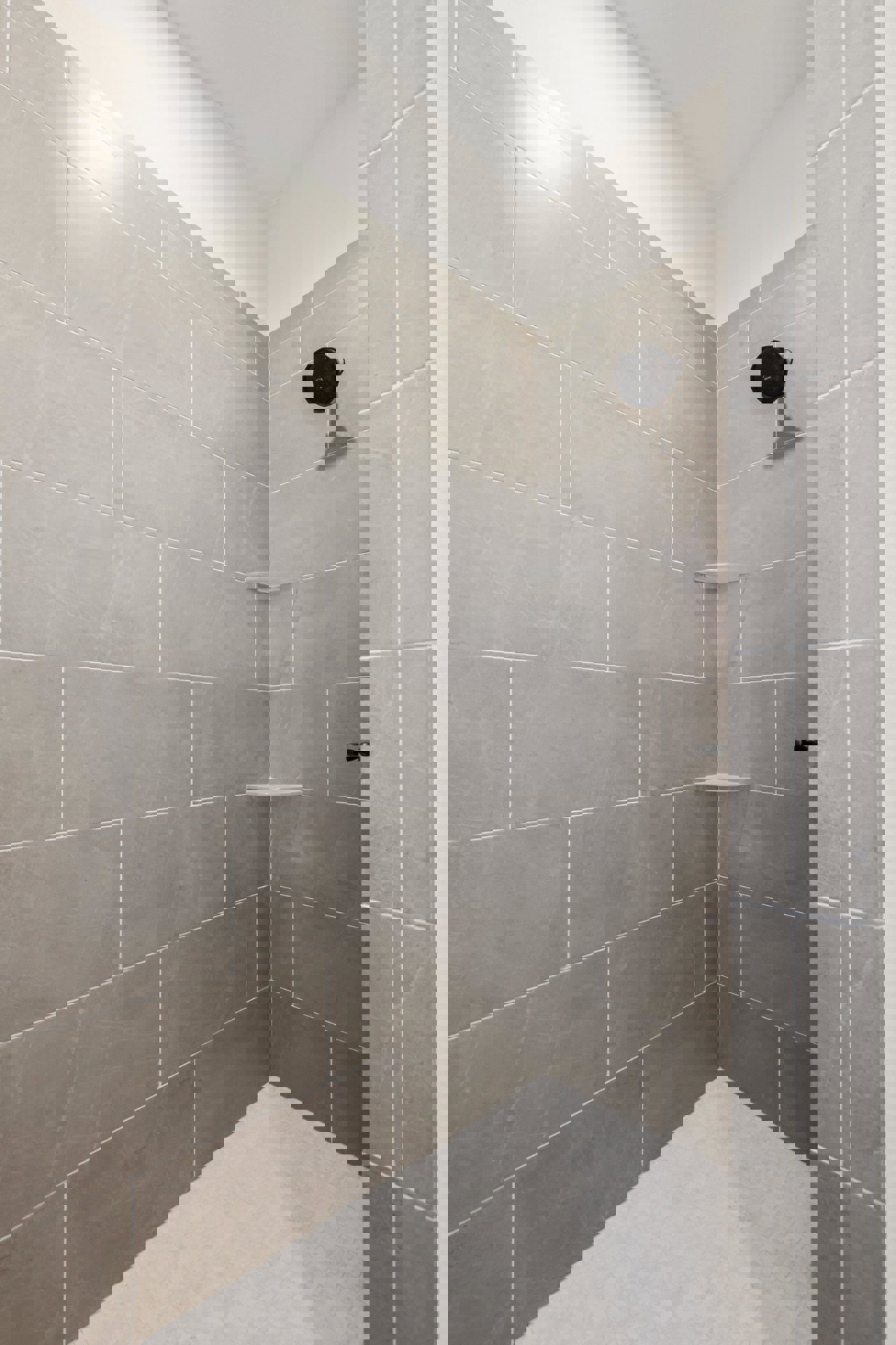 Black shower head mounted on a marble tile wall above a matching tile floor in a modern bathroom