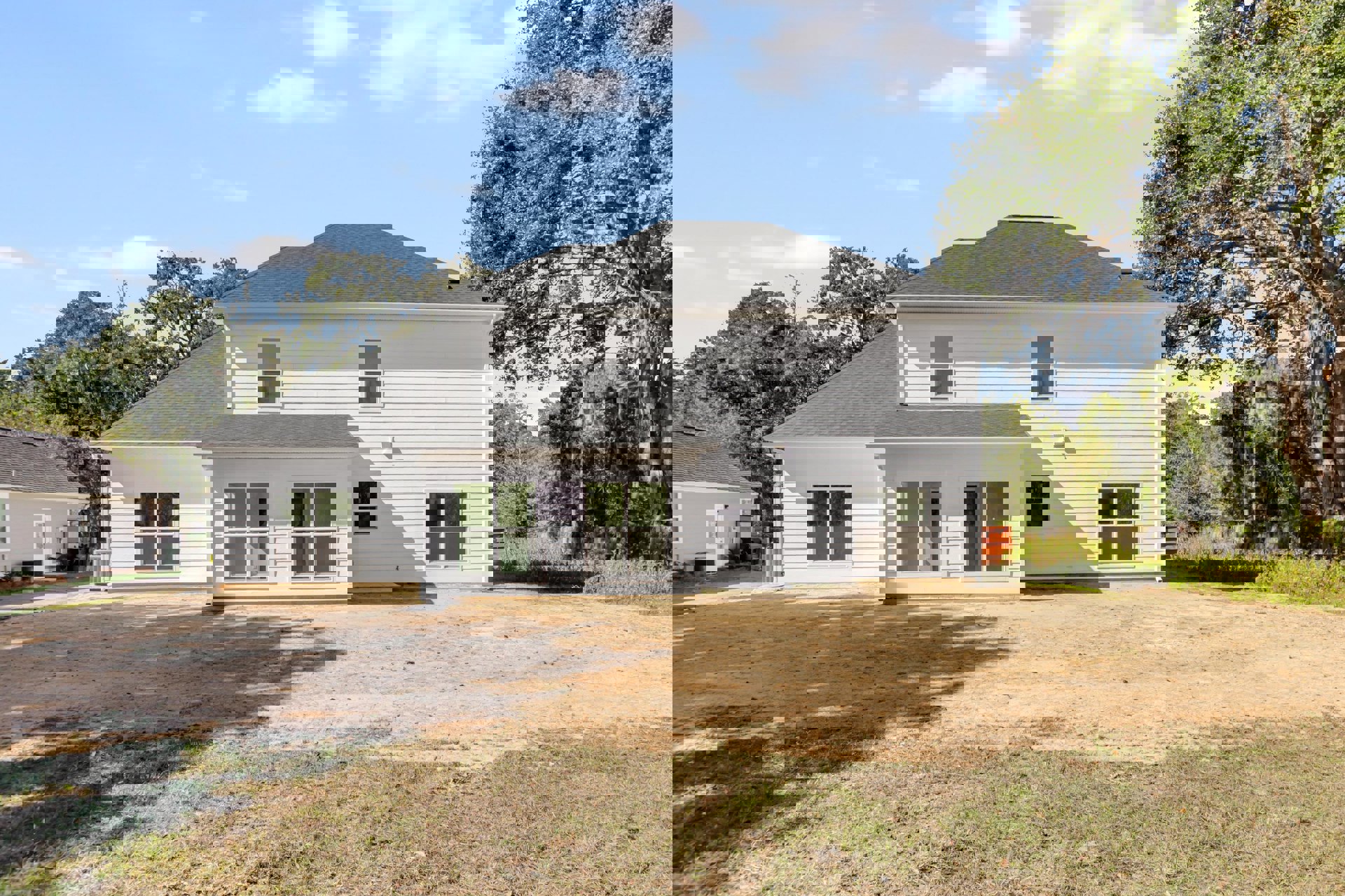White house with grey roof, expansive green lawn, white-framed windows, mature tree beside the building, partly cloudy sky overhead