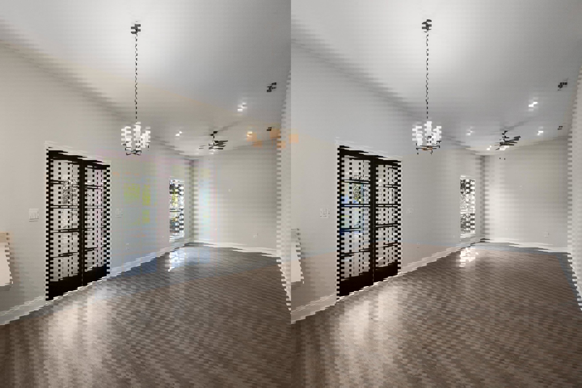 Spacious room with wood flooring, white plaster walls, ceiling fan, chandelier, double glass-paneled doors, and large window allowing natural light