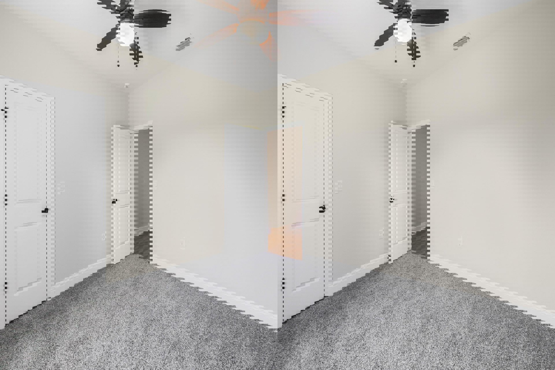 Carpeted room with white walls, ceiling fan with light, open white door featuring black handle, and visible light switch.