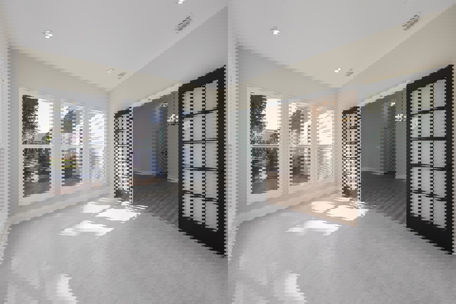 White-walled room featuring a large window and a black door with white frosted glass panels, light wood flooring, and minimal decor