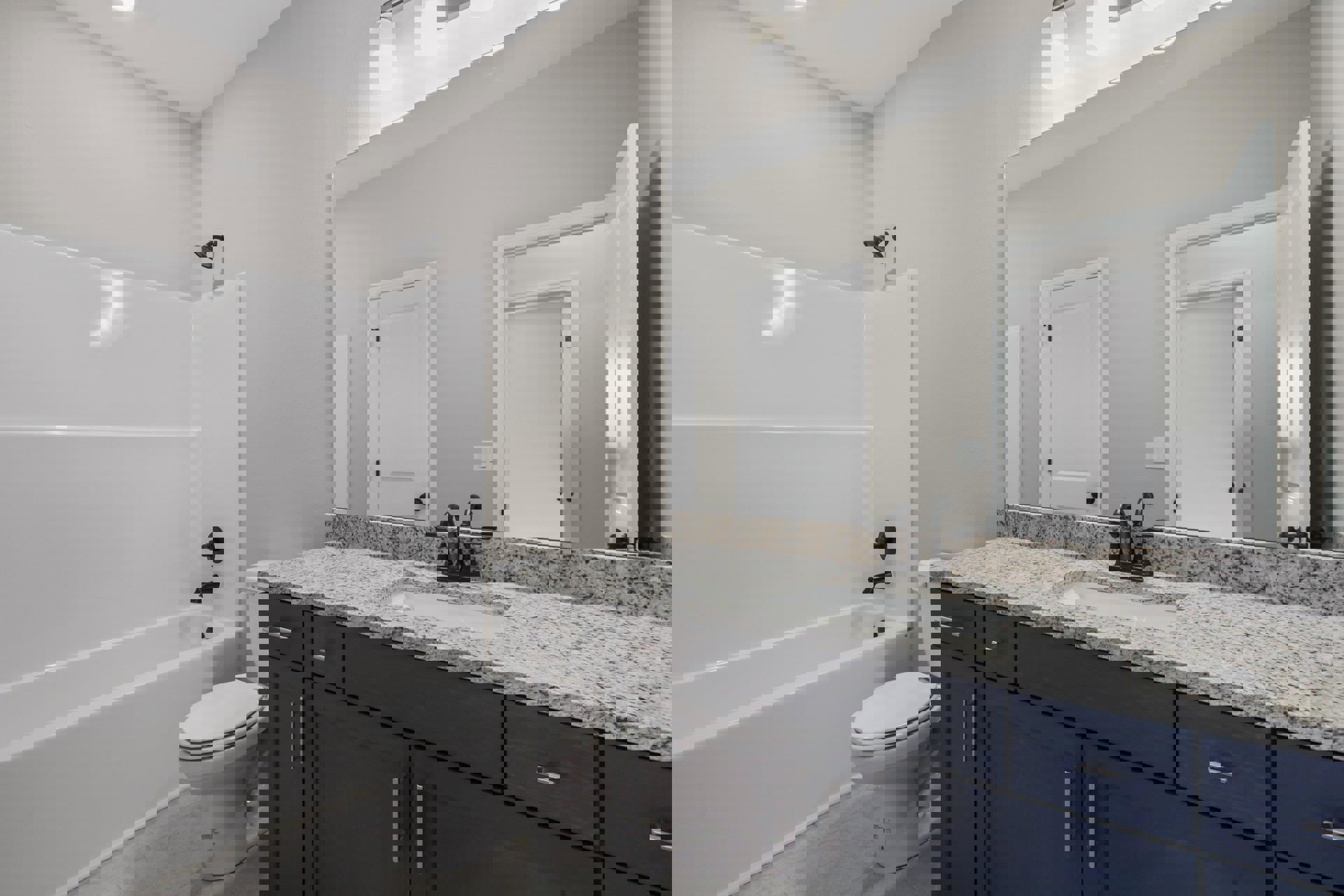 Modern bathroom featuring a white bathtub, white toilet with seat down, black shower head, white tile walls, white door with black handle, and light cabinetry with stone countertop