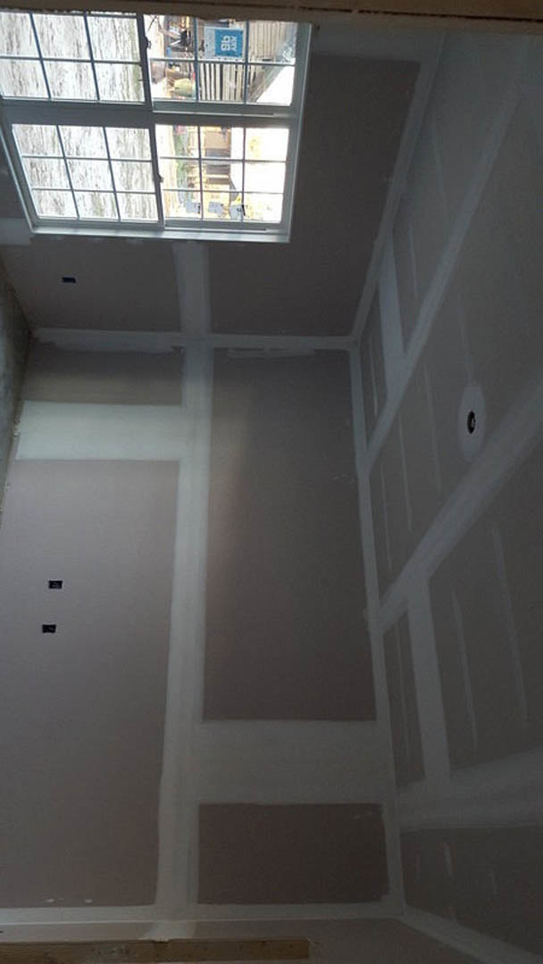 White plaster wall with multi-pane window, decorative molding, and natural daylight illuminating the interior room