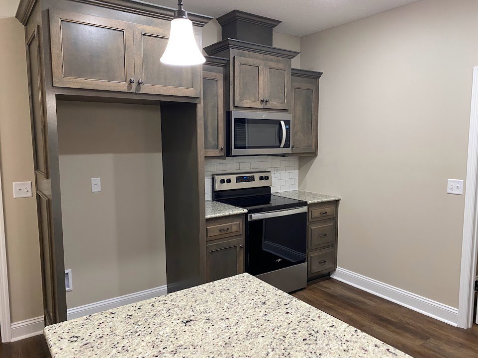 Marble countertop kitchen featuring open microwave oven, stainless steel stove, white cabinetry, wall outlet, and modern lighting fixture