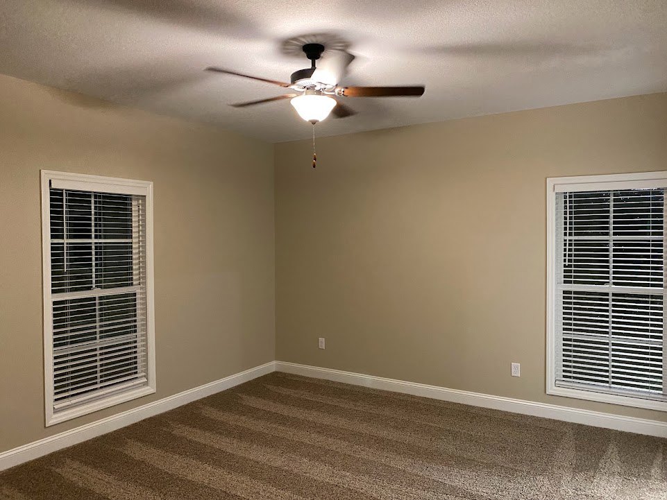 Ceiling fan with illuminated light fixture mounted on white plaster ceiling, window with closed blinds, carpeted floor, neutral painted walls