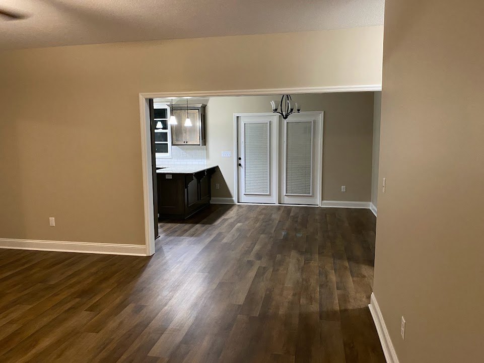 Open-concept room featuring hardwood floors, white walls, a kitchen island with marble countertop, white door with blinds, and a chandelier.