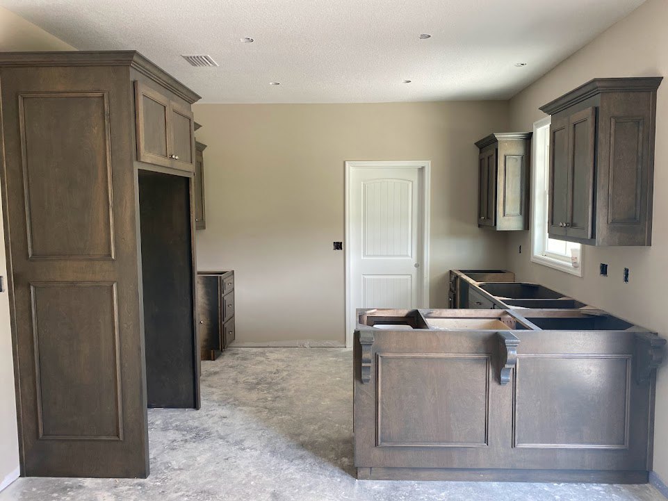 Modern kitchen featuring white shaker cabinets, a white door with black hardware, light wood flooring, and a black chalkboard framed in white above a metal-trimmed wood panel.