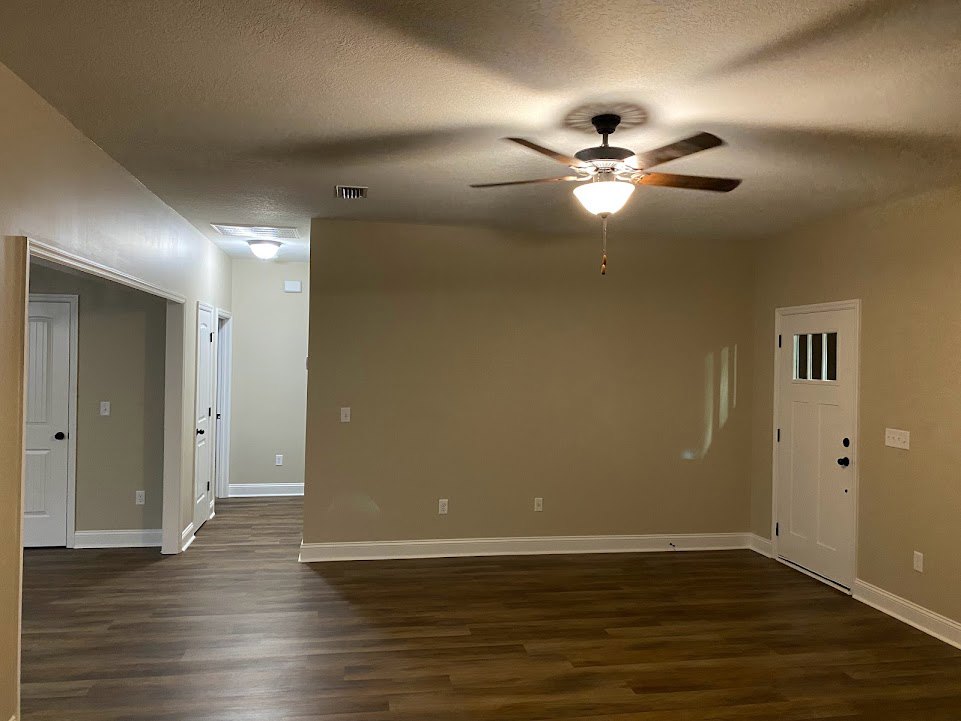 Ceiling fan with light fixture mounted on white plaster ceiling, wood laminate flooring with white trim, white door featuring black handle and knob