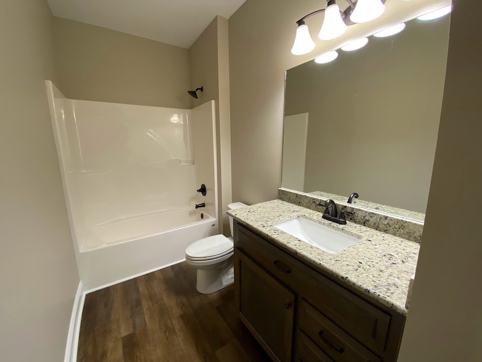 Marble countertop with white undermount sink, chrome faucet, freestanding bathtub, white toilet, tile flooring, recessed ceiling lights, light wood cabinetry