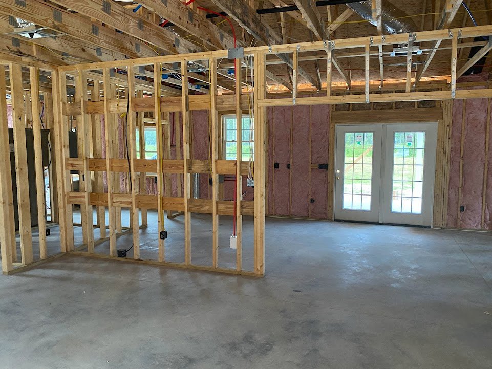Unfinished room with exposed wood framing, concrete floor, white double doors with glass panes, and a multi-pane window