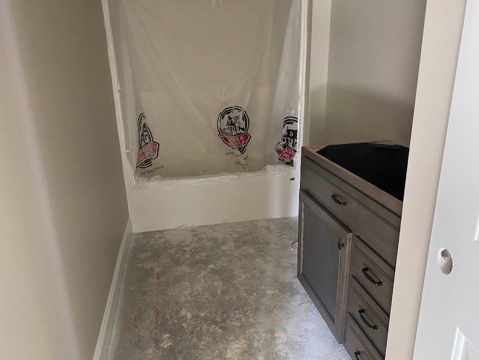 Bathroom with white plastic wall covering, grey tile floor, black cabinet drawer, glass panel, and white cabinetry.