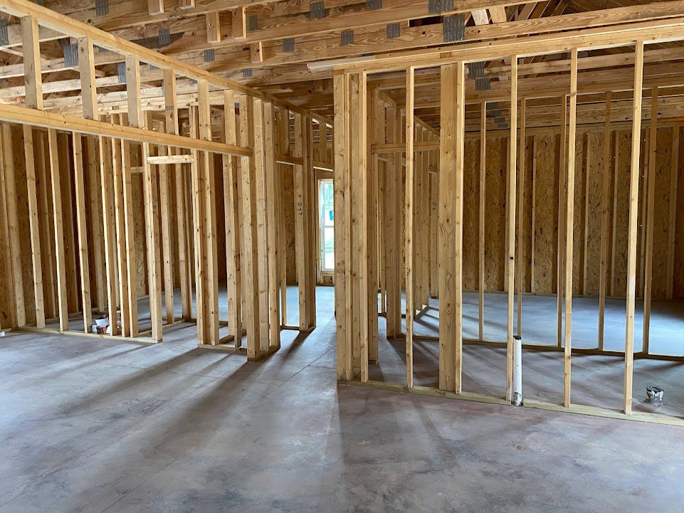 Wood-framed room under construction with exposed beams, studs, and unfinished ceiling and floor