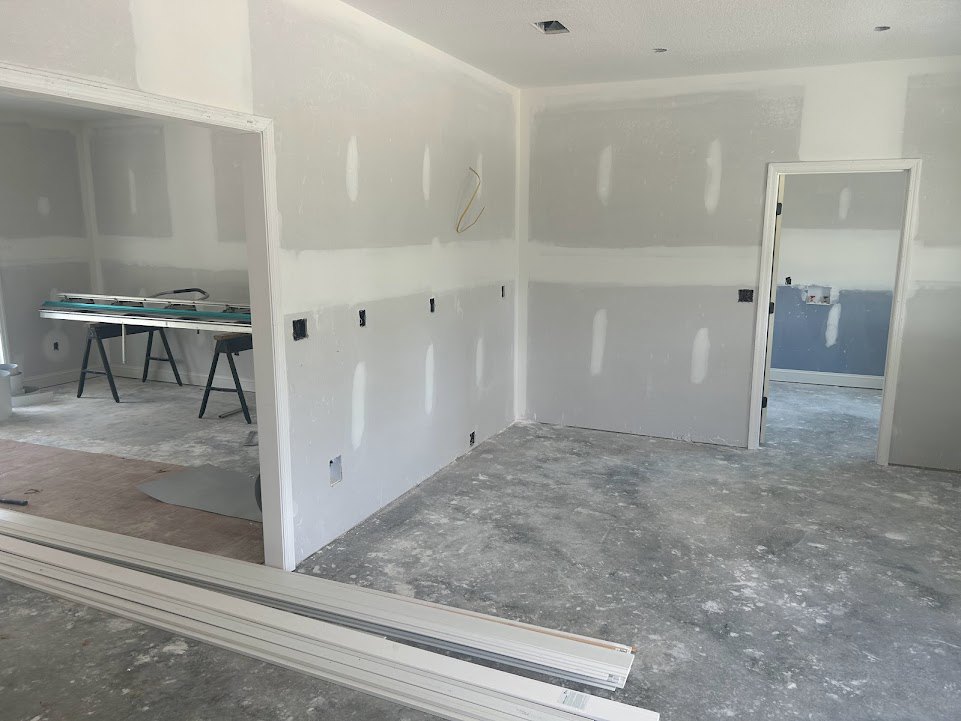 White walls and ceiling, white door with glass panel, concrete floor, black wooden chair legs, table with slender legs.