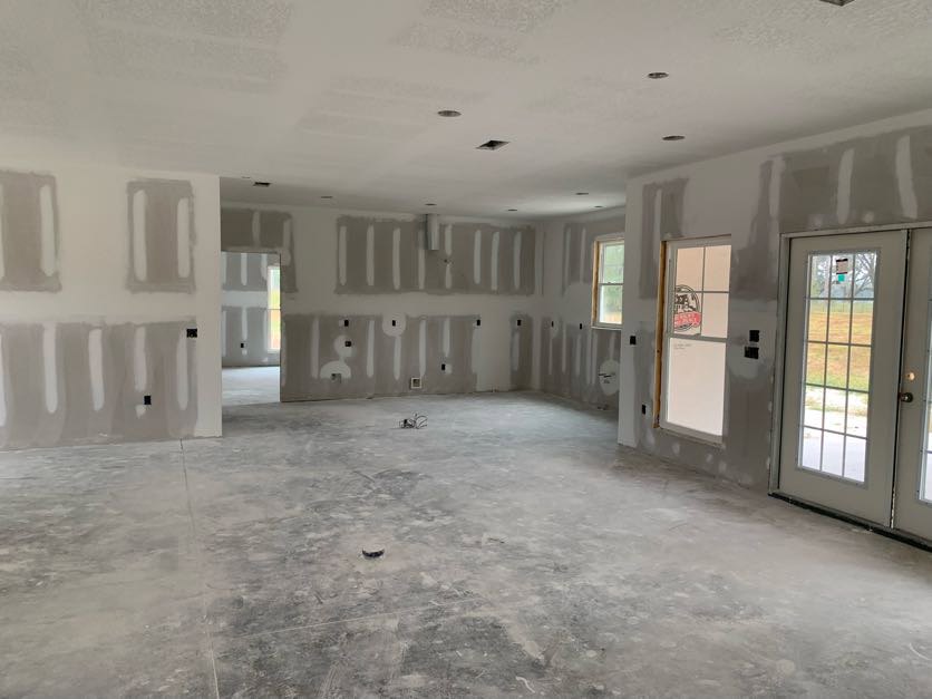 White-walled room with glass-paneled door, concrete floor, window overlooking grassy field, and whiteboard displaying a picture.