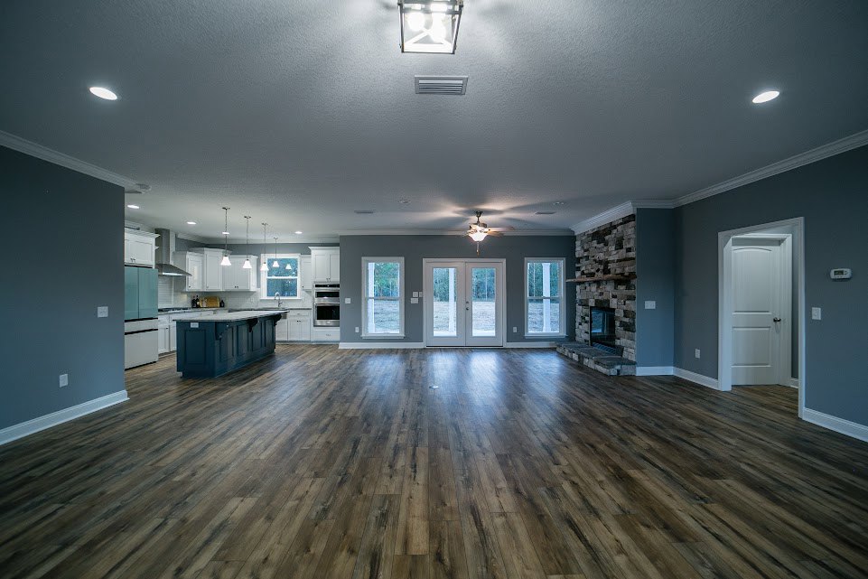 Spacious living area with hardwood flooring, stone fireplace, double glass-paneled doors, blue kitchen island with white countertops, white door with silver handle, and window with