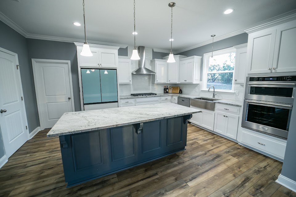 Spacious kitchen featuring a large white marble island, stainless steel oven, glass door with illuminated panels, cabinetry, and a window overlooking trees.
