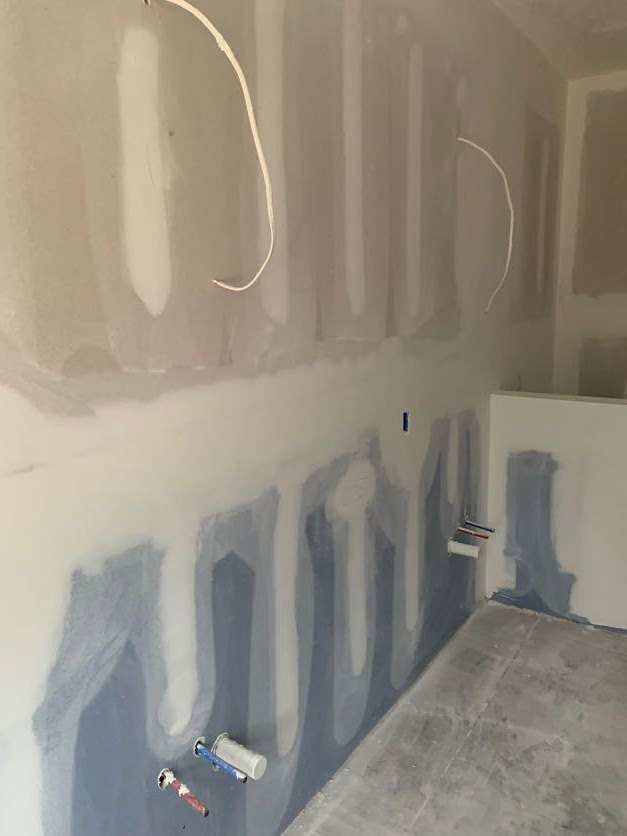 White and blue painted plaster wall with visible crack, concrete floor, indoor residential room