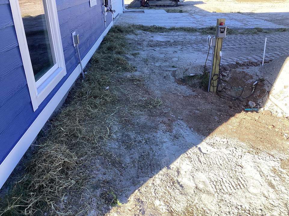 Blue house with white-framed window, grassy and dirt-covered yard with visible tire tracks, close-up views of pipe, power box, and window