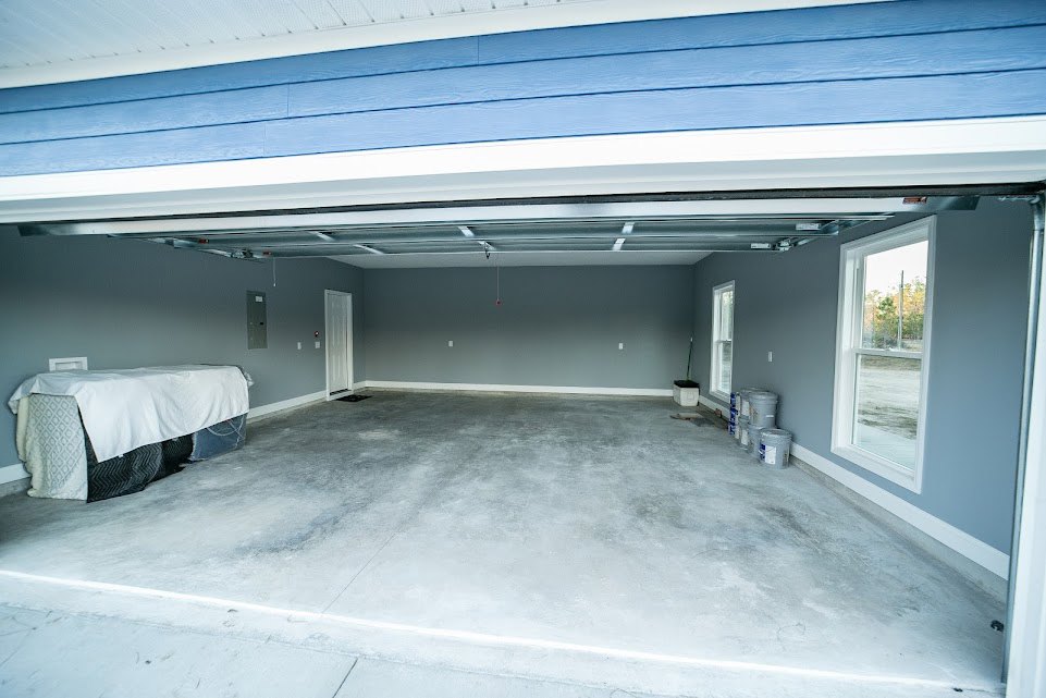 Garage interior featuring blue-painted wall, white sheet draped over an object, concrete floor, and window with tree views