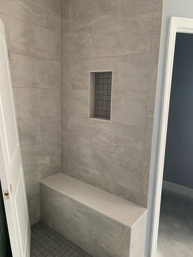 Walk-in shower with marble tile walls, built-in bench, glass enclosure, and plaster ceiling in modern bathroom.