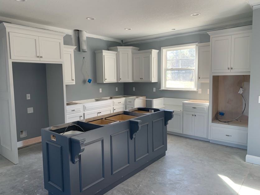 White kitchen cabinets, blue island with drawers, white-framed window, white pillar with black border, light countertops, stainless steel sink, hardwood flooring, ceiling lights