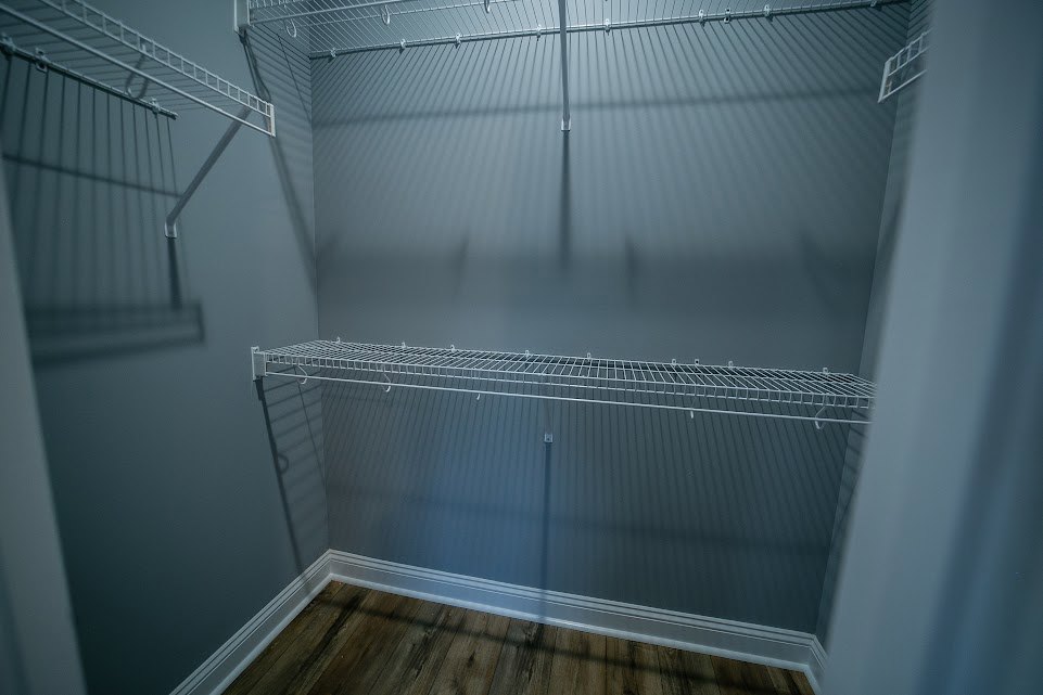 Closet with white wire shelves, metal hanging rod, and wood flooring with white baseboard trim