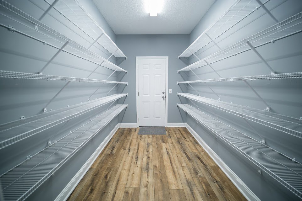 White paneled door with silver knobs, wood floor with a dark mat, built-in wall shelves, plaster walls, ceiling light fixture