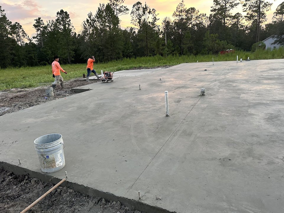 Workers pouring and smoothing concrete slab on construction site, grassy area and trees in background, Diana, Princess of Wales Memorial Fountain visible beyond work zone