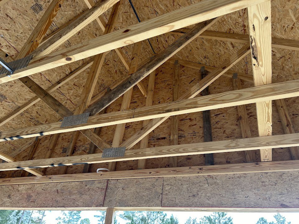 Exposed wooden roof trusses and beams with natural wood finish, window framed in wood, metal hardware visible on structural elements