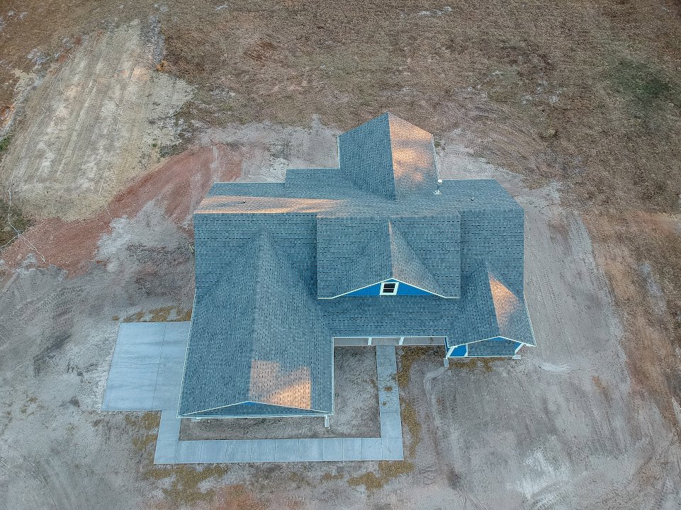 Two-story custom home with blue metal roof, white siding, and paved driveway surrounded by landscaped lawn