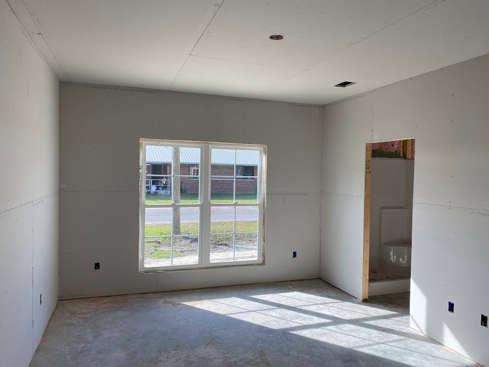 Bathroom with white walls, wooden window frame, concrete floor, ceiling light, and window overlooking a house and grassy yard