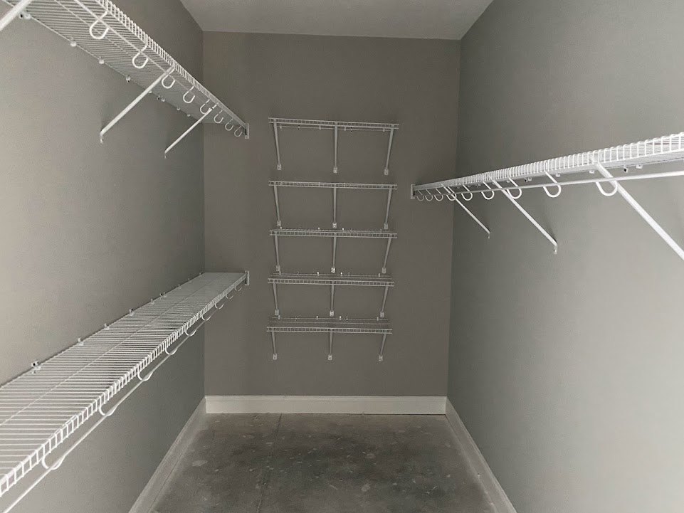 Closet with white wire shelves mounted on walls, concrete floor, and metal shelving on ceiling