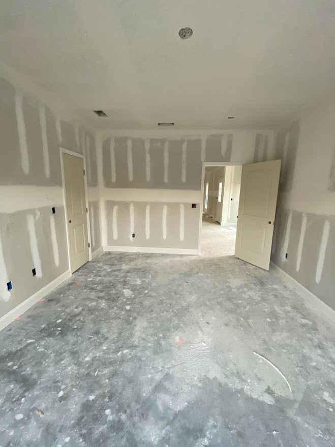 White-walled room with white-painted door featuring a silver knob, grey marble floor, and smooth plaster ceiling