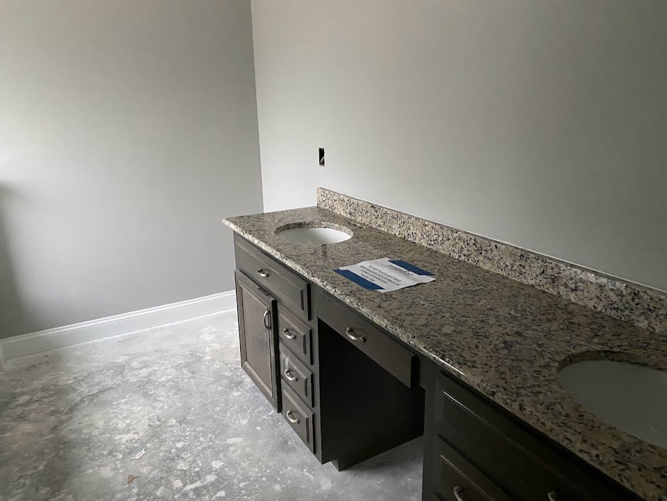 Bathroom with granite countertop, dual sinks, white cabinetry drawers, chrome faucets, and white walls.