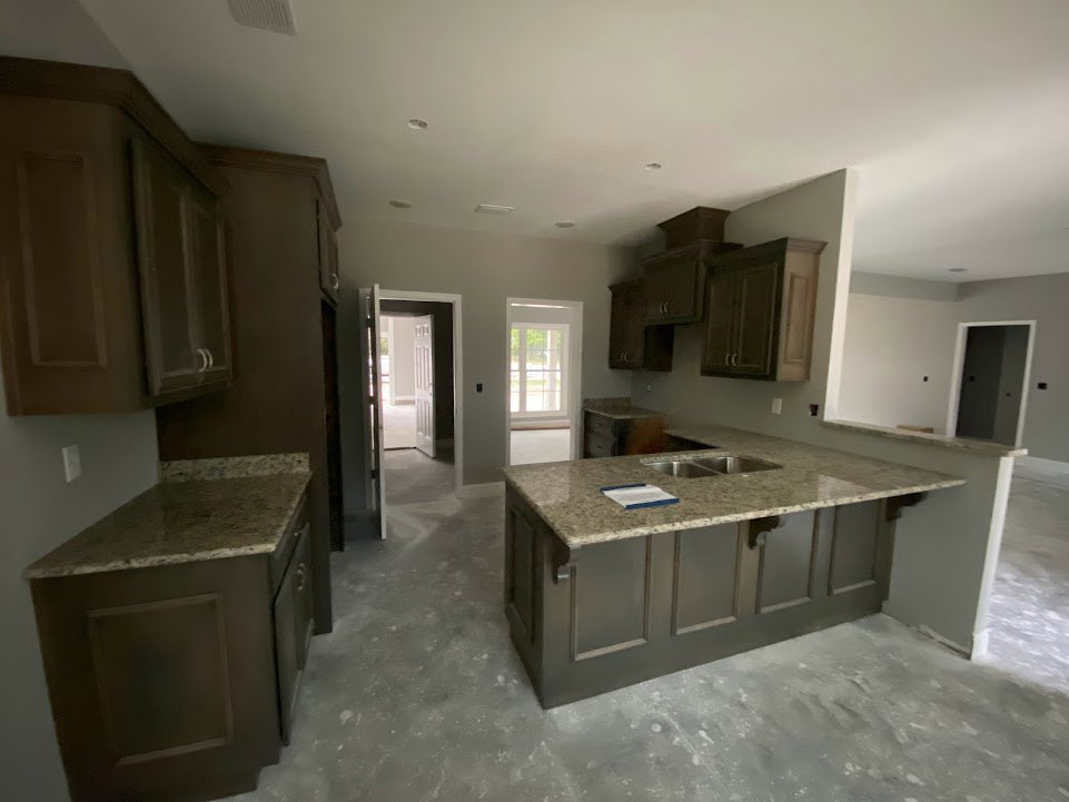 Granite kitchen countertops with undermount sink, white cabinetry, window with white frame, and white door featuring black hardware