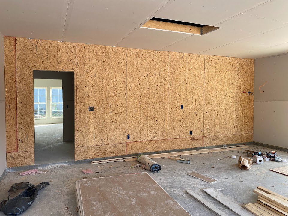 Unfinished room with white plaster walls, large window with white frame, concrete floor, black plastic bag, and rolled carpet on the ground