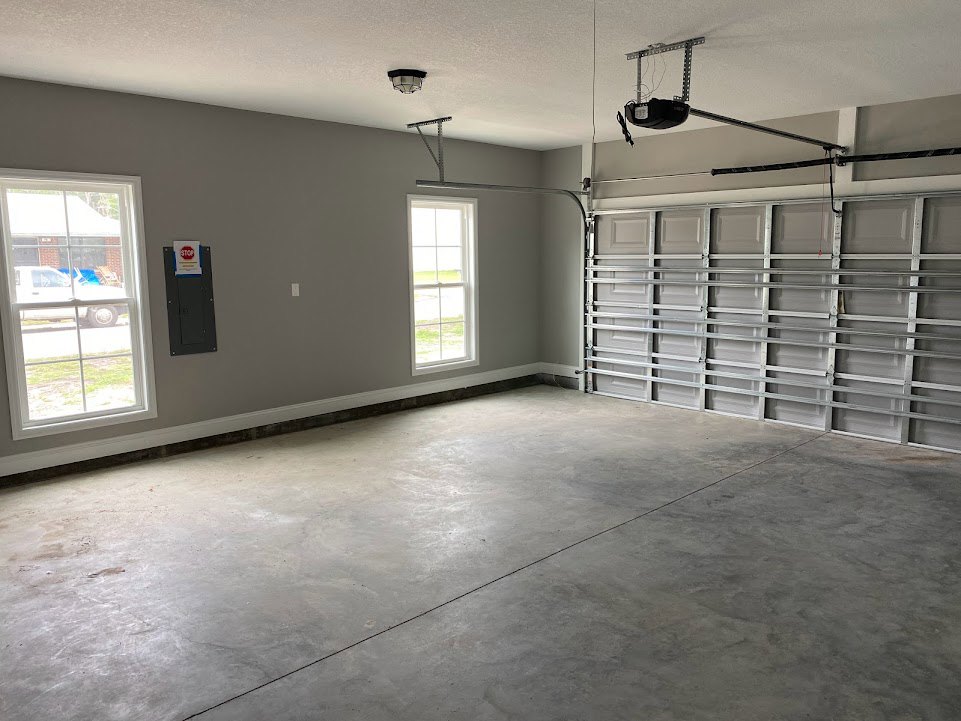 Garage interior with concrete floor showing a visible crack, white-framed window overlooking a parked car, metal shelving along the wall, and closed garage door