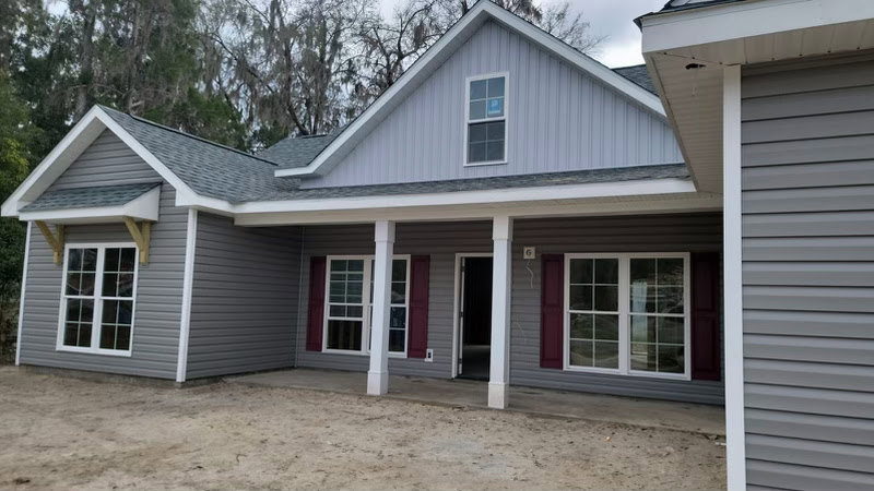 Two-story home with white siding, multi-pane windows, open front door, covered porch, and paved driveway.