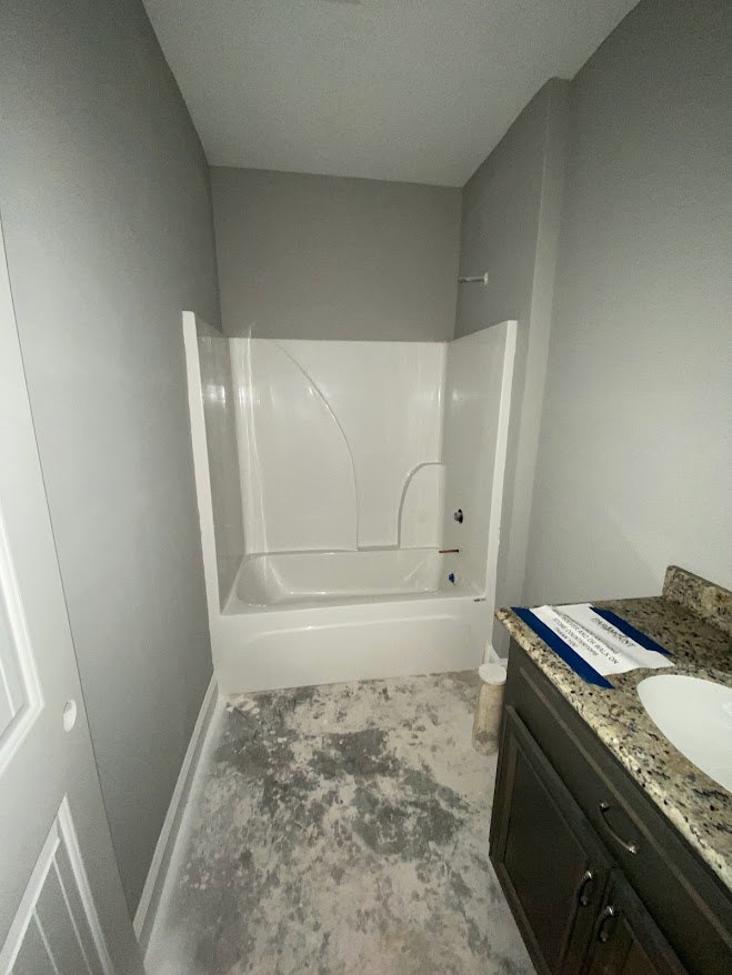 Bathroom with white freestanding bathtub, marble countertop sink, blue accent sign, and grey and white tiled floor