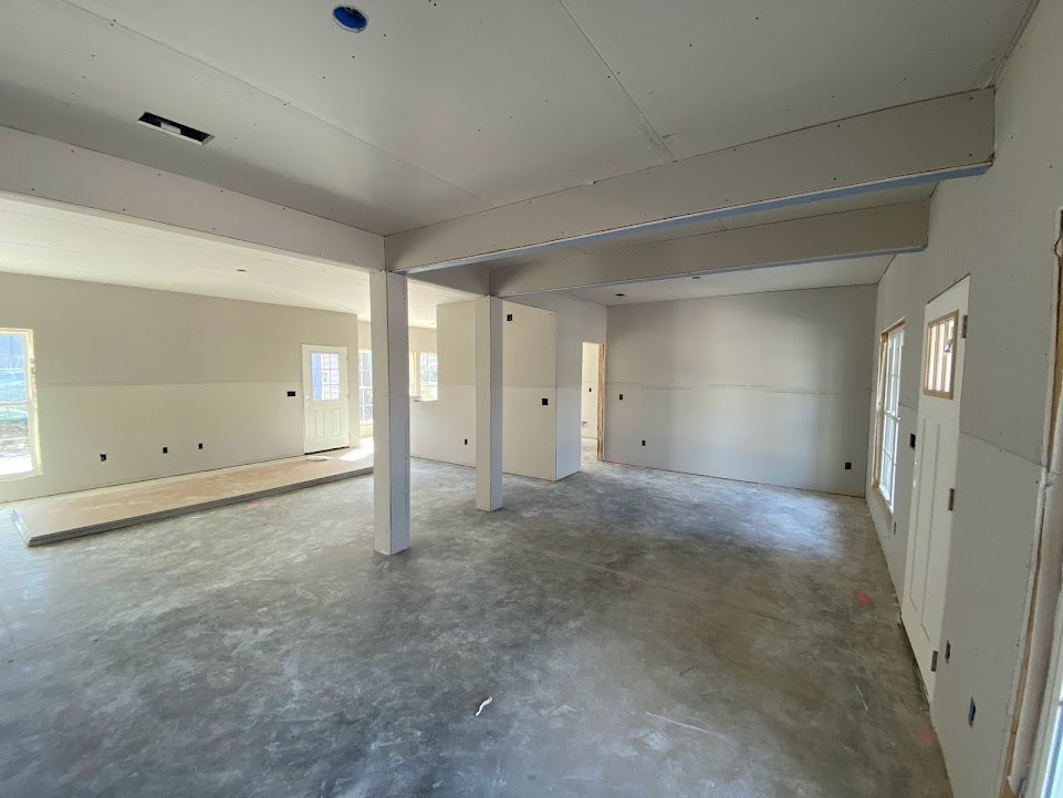 Modern room with smooth white walls, polished concrete floor, white ceiling with recessed lighting, and structural pillars