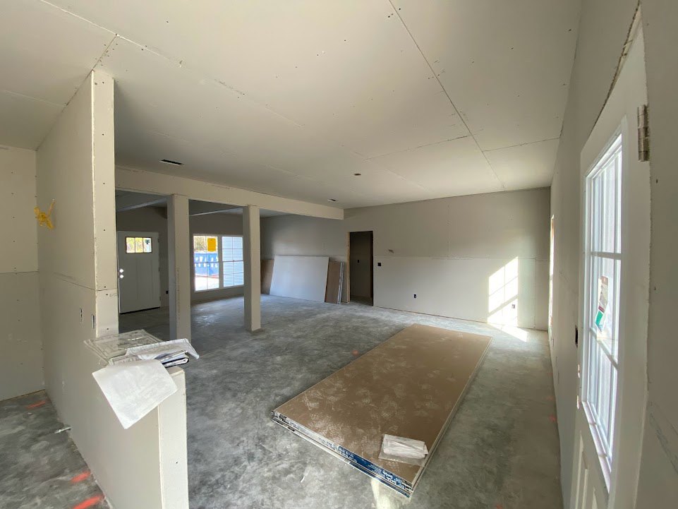 Spacious room with light wood flooring, oversized neutral carpet, white walls, large window with trim, and a door featuring a glass pane