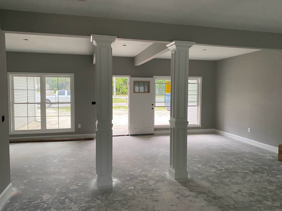 White-painted columns and door in a bright room with plaster walls, light flooring, and a window showing a white truck outside.
