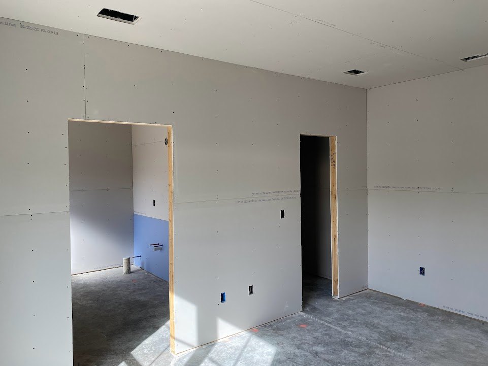 Concrete floor with central metal pole, black accent wall featuring white-framed doorway, adjacent light blue and white walls, white surface with scattered black dots, plaster