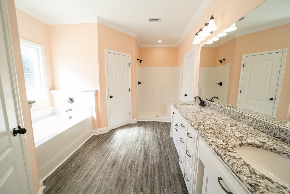 Bathroom with pink plaster walls, black and white marble countertop, white sink, wood flooring, white door with black knob, window letting in natural light