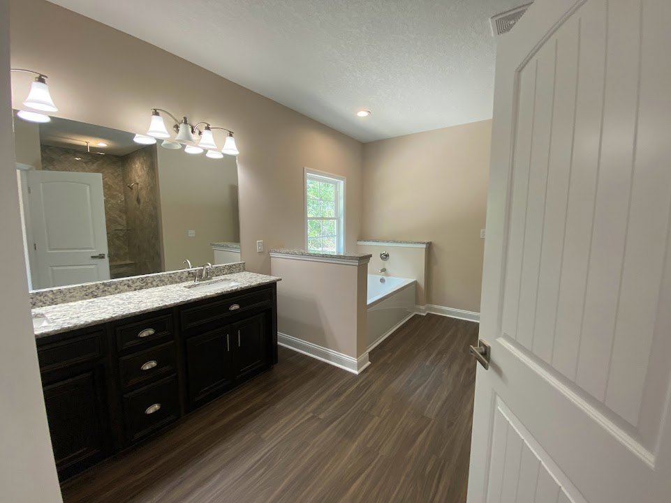 Bathroom with freestanding tub, marble countertop vanity, white framed window, white doors with silver hardware, light fixture with white shade, tile flooring, and white cabinetry.