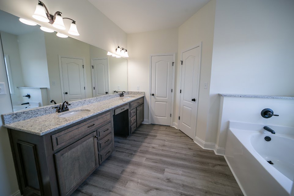 Bathroom featuring a marble countertop, white cabinetry with black knobs, a freestanding bathtub, wall-mounted mirror above the sink, and a row of modern light fixtures.