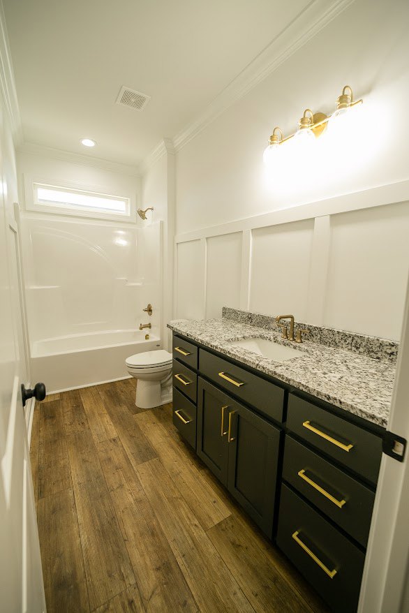 Modern bathroom featuring white ceramic sink with chrome faucet, matching toilet, light gray tile flooring, wood cabinetry with drawers, and stone countertop.