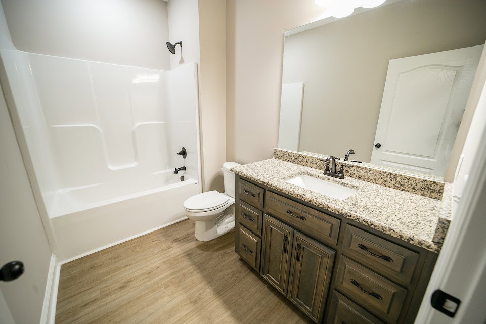 Bathroom with white sink and black faucet, white toilet, built-in cabinets, white bathtub, tiled walls, and white door with black handle